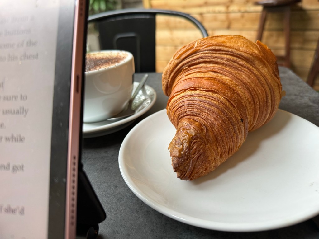 An iPad, croissant and coffee in a cafe table. 